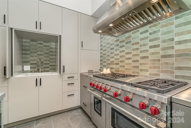 kitchen featuring range with two ovens, sink, decorative backsplash, white cabinetry, and wall chimney range hood