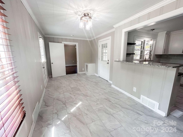 interior space featuring hanging light fixtures, stone counters, light tile patterned floors, crown molding, and kitchen peninsula