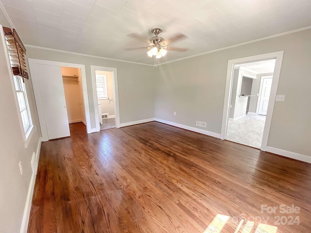 unfurnished bedroom featuring hardwood / wood-style floors, a spacious closet, ensuite bathroom, ceiling fan, and crown molding