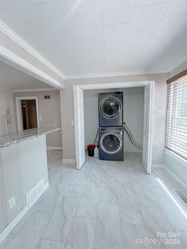 clothes washing area with light tile patterned floors, stacked washing maching and dryer, and crown molding