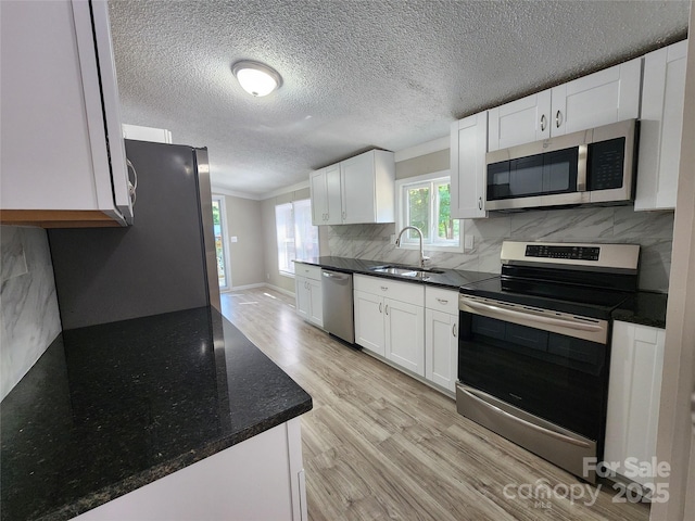 kitchen with stainless steel appliances, sink, light hardwood / wood-style flooring, and white cabinets