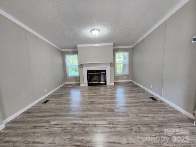 unfurnished living room featuring crown molding, a textured ceiling, light hardwood / wood-style flooring, and a wealth of natural light