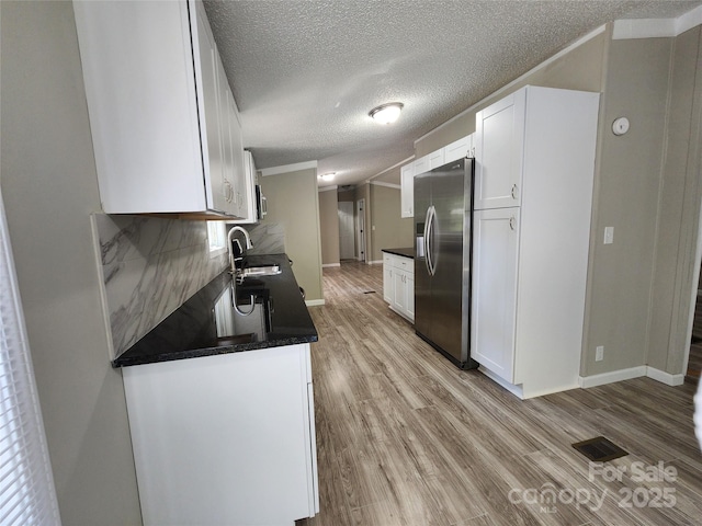 kitchen with stainless steel refrigerator with ice dispenser, sink, white cabinets, and light hardwood / wood-style flooring