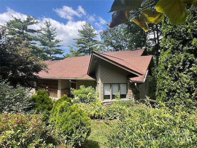 view of side of property featuring stone siding and a shingled roof