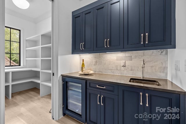 bar with sink, light wood-type flooring, tasteful backsplash, beverage cooler, and blue cabinetry