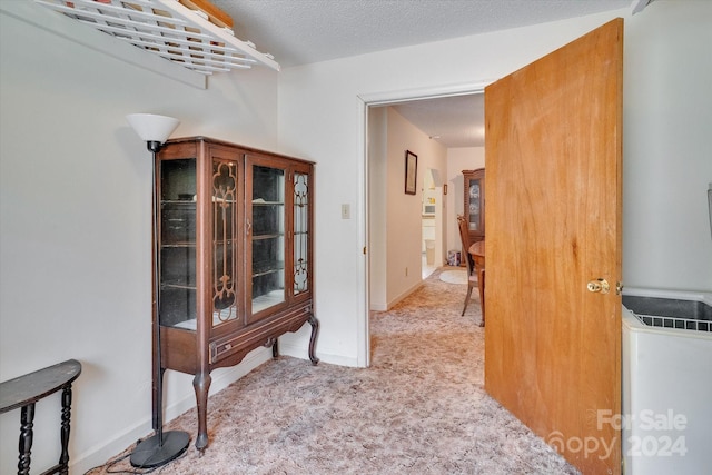 hallway featuring a textured ceiling and light carpet