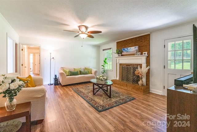 living room featuring ceiling fan, light wood-type flooring, a textured ceiling, and a brick fireplace