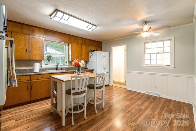 kitchen featuring ceiling fan, wood-type flooring, sink, a textured ceiling, and crown molding