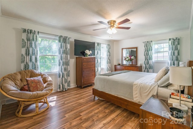 bedroom featuring ceiling fan, hardwood / wood-style floors, ornamental molding, and multiple windows