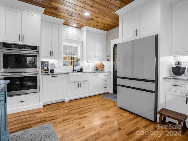 kitchen with light wood-type flooring, a sink, appliances with stainless steel finishes, white cabinets, and decorative backsplash