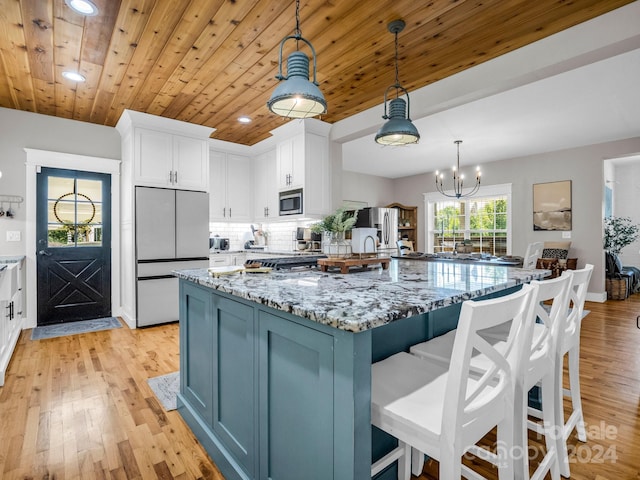 kitchen featuring appliances with stainless steel finishes, dark stone counters, wood ceiling, decorative light fixtures, and light hardwood / wood-style floors