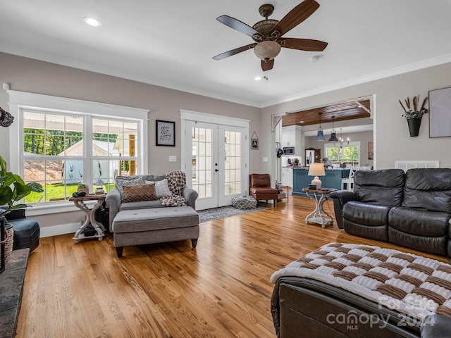 living room with french doors, ceiling fan with notable chandelier, light hardwood / wood-style flooring, and plenty of natural light