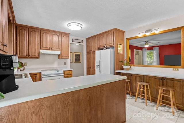 kitchen with light tile patterned floors, white refrigerator with ice dispenser, range, ceiling fan, and kitchen peninsula