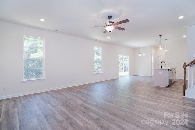 unfurnished living room featuring ceiling fan, light wood-type flooring, sink, and a healthy amount of sunlight