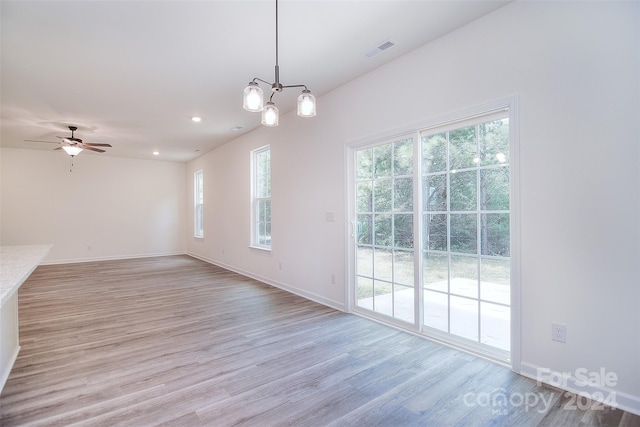 spare room with light wood-type flooring, ceiling fan with notable chandelier, and plenty of natural light