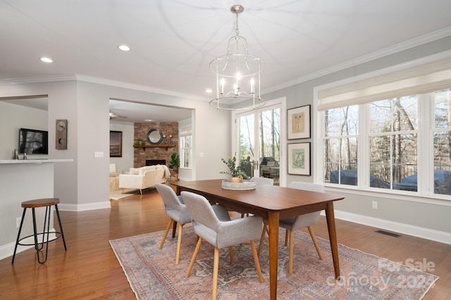 dining space featuring a fireplace, hardwood / wood-style floors, a notable chandelier, and ornamental molding