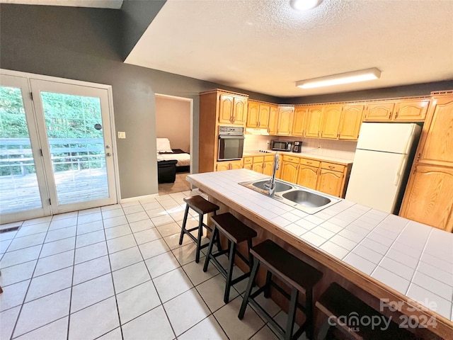 kitchen with white refrigerator, tile countertops, sink, stainless steel oven, and a breakfast bar area