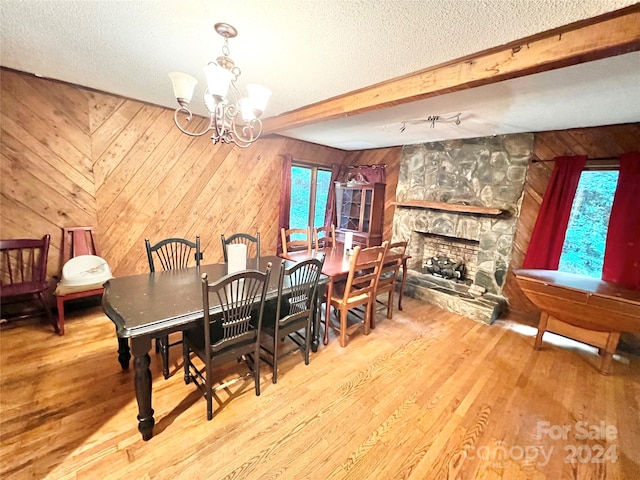 dining area with a textured ceiling, hardwood / wood-style floors, a stone fireplace, and beamed ceiling