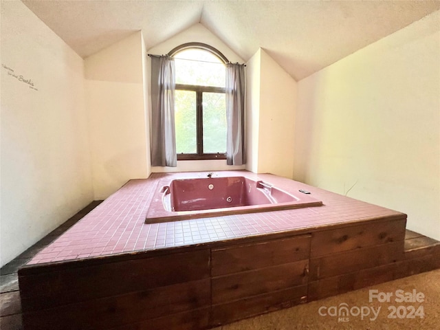 bathroom with a tub, a textured ceiling, and vaulted ceiling