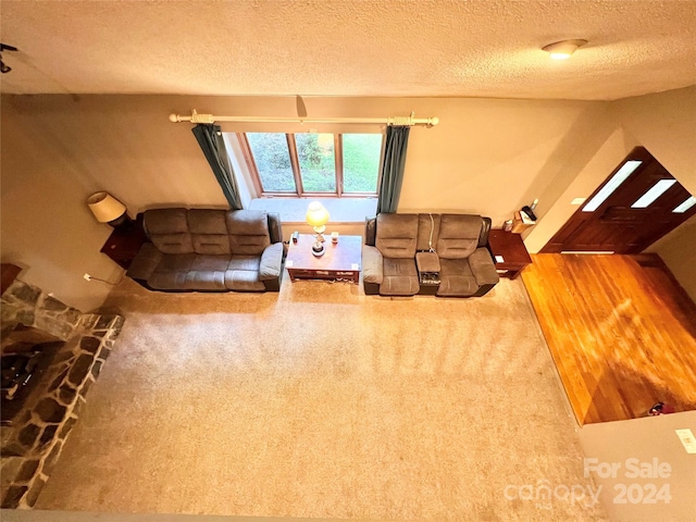 living room featuring a textured ceiling, hardwood / wood-style floors, and a stone fireplace