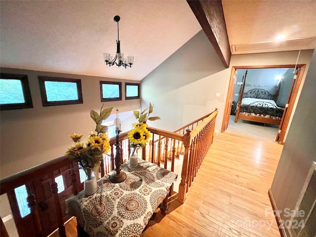 stairs featuring hardwood / wood-style floors, a textured ceiling, a notable chandelier, and vaulted ceiling with beams