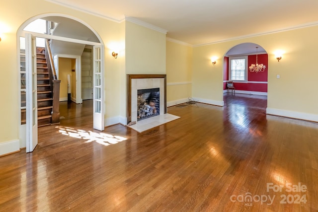 unfurnished living room featuring a tiled fireplace, dark wood-type flooring, ornamental molding, and a chandelier