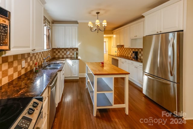 kitchen with dark stone counters, appliances with stainless steel finishes, white cabinets, and hanging light fixtures