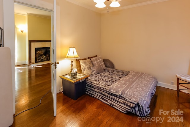 bedroom with crown molding, ceiling fan, a tiled fireplace, and wood-type flooring