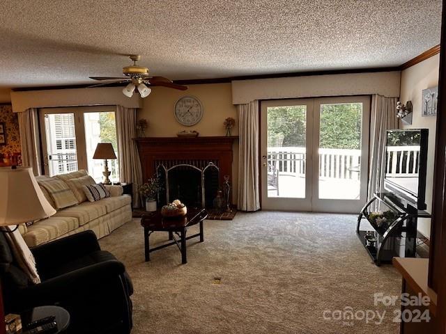 carpeted living room with a brick fireplace, ceiling fan, a healthy amount of sunlight, and a textured ceiling