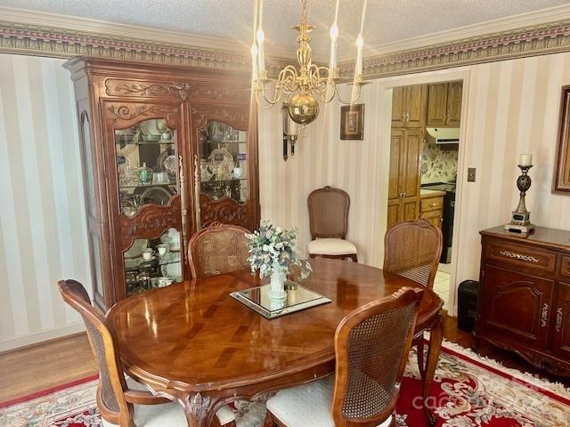 dining space with light hardwood / wood-style flooring, a textured ceiling, crown molding, and an inviting chandelier