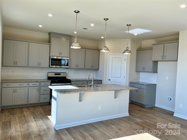 kitchen with appliances with stainless steel finishes, hardwood / wood-style floors, a kitchen bar, and tasteful backsplash