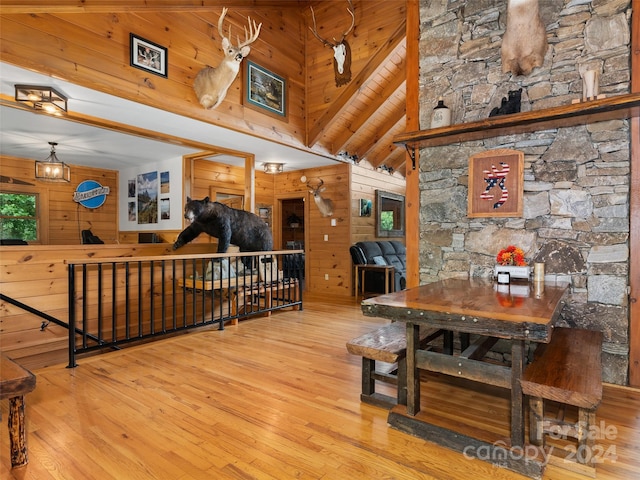 dining space featuring beamed ceiling, high vaulted ceiling, light hardwood / wood-style flooring, and wooden walls