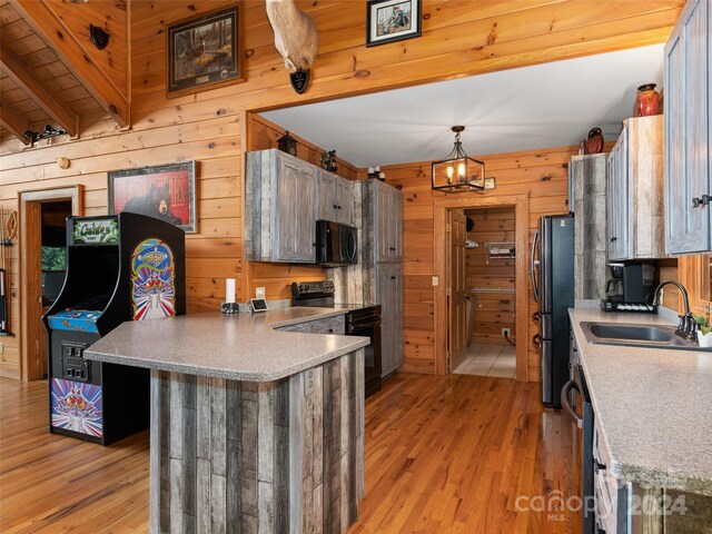 kitchen with wood walls, sink, light wood-type flooring, hanging light fixtures, and black appliances