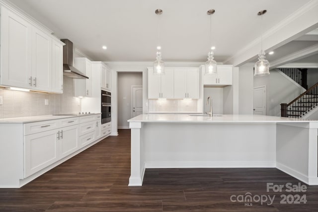 kitchen with sink, pendant lighting, wall chimney exhaust hood, white cabinets, and dark wood-type flooring