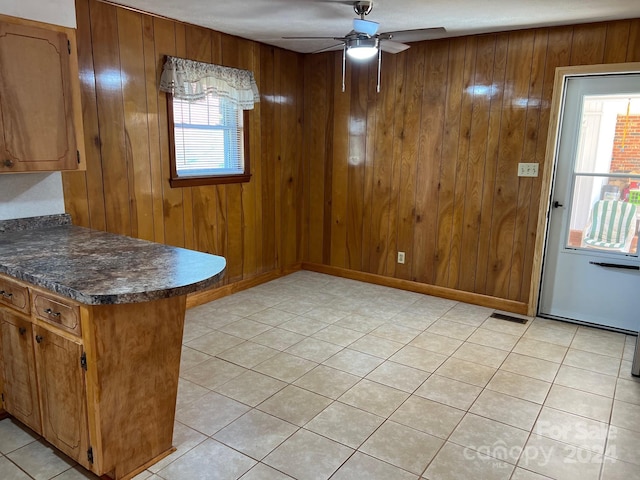 unfurnished dining area featuring light tile patterned floors, ceiling fan, and wood walls