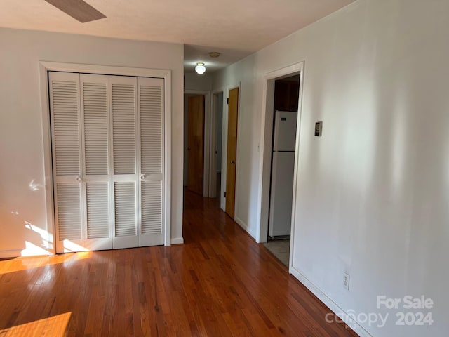 unfurnished bedroom featuring dark hardwood / wood-style flooring, ceiling fan, a closet, and white refrigerator