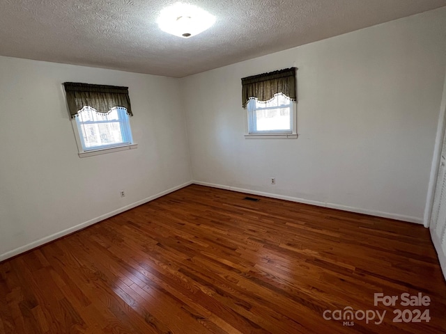 unfurnished room with a textured ceiling, dark hardwood / wood-style flooring, and a wealth of natural light