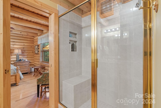 bathroom with beamed ceiling, hardwood / wood-style floors, a shower with shower door, and rustic walls