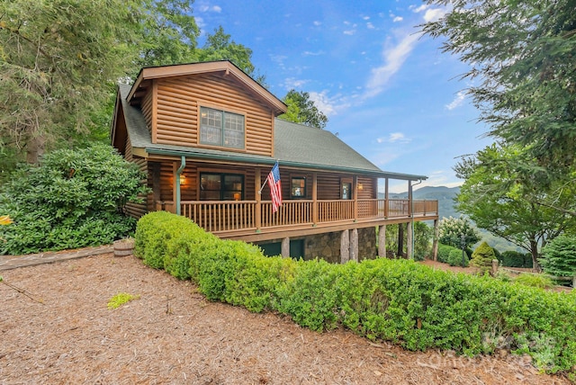 rear view of property with stone siding, roof with shingles, and faux log siding