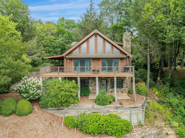 back of property featuring a deck, stone siding, a patio, log siding, and a chimney