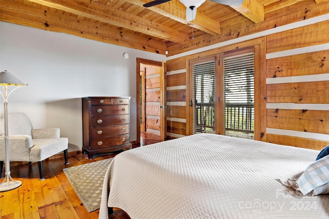 bedroom with beamed ceiling, hardwood / wood-style floors, access to exterior, ceiling fan, and wooden walls