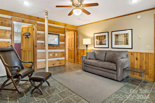 carpeted living room with wood walls, ceiling fan, and crown molding