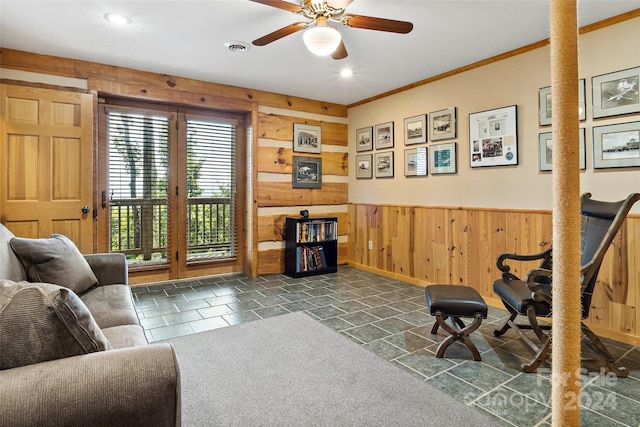 interior space featuring ceiling fan, dark colored carpet, wooden walls, and ornamental molding