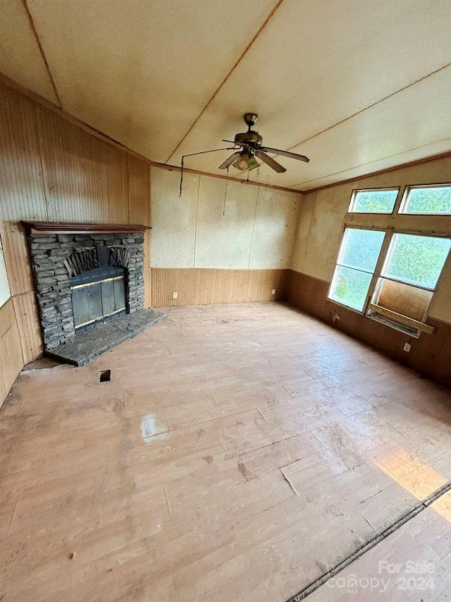 unfurnished living room with ceiling fan, a stone fireplace, and wood-type flooring