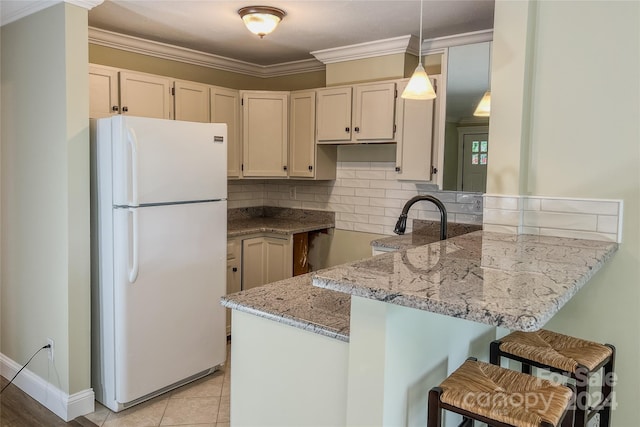 kitchen with decorative backsplash, ornamental molding, pendant lighting, a breakfast bar, and white refrigerator