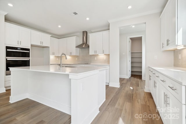 kitchen with black appliances, white cabinetry, sink, a center island with sink, and wall chimney exhaust hood