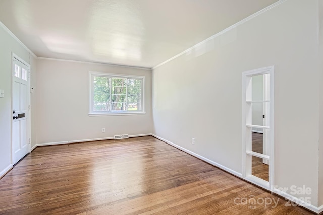 empty room featuring baseboards, wood finished floors, visible vents, and crown molding