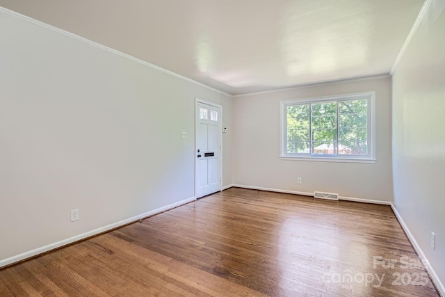 empty room featuring ornamental molding, wood finished floors, visible vents, and baseboards