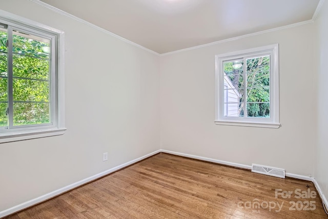 unfurnished room with baseboards, visible vents, wood finished floors, and ornamental molding