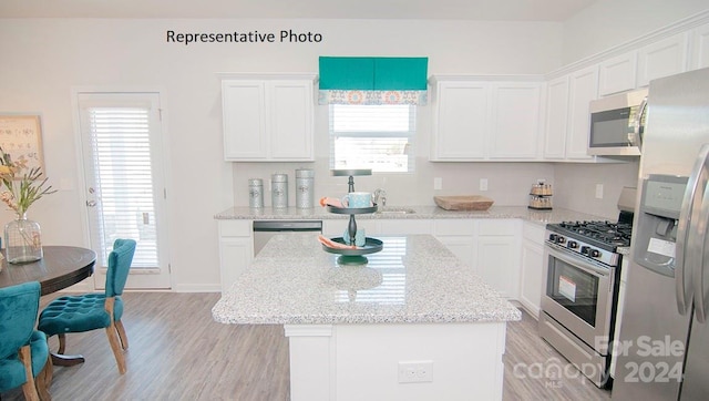 kitchen with light stone counters, light hardwood / wood-style floors, a kitchen island, stainless steel appliances, and white cabinets